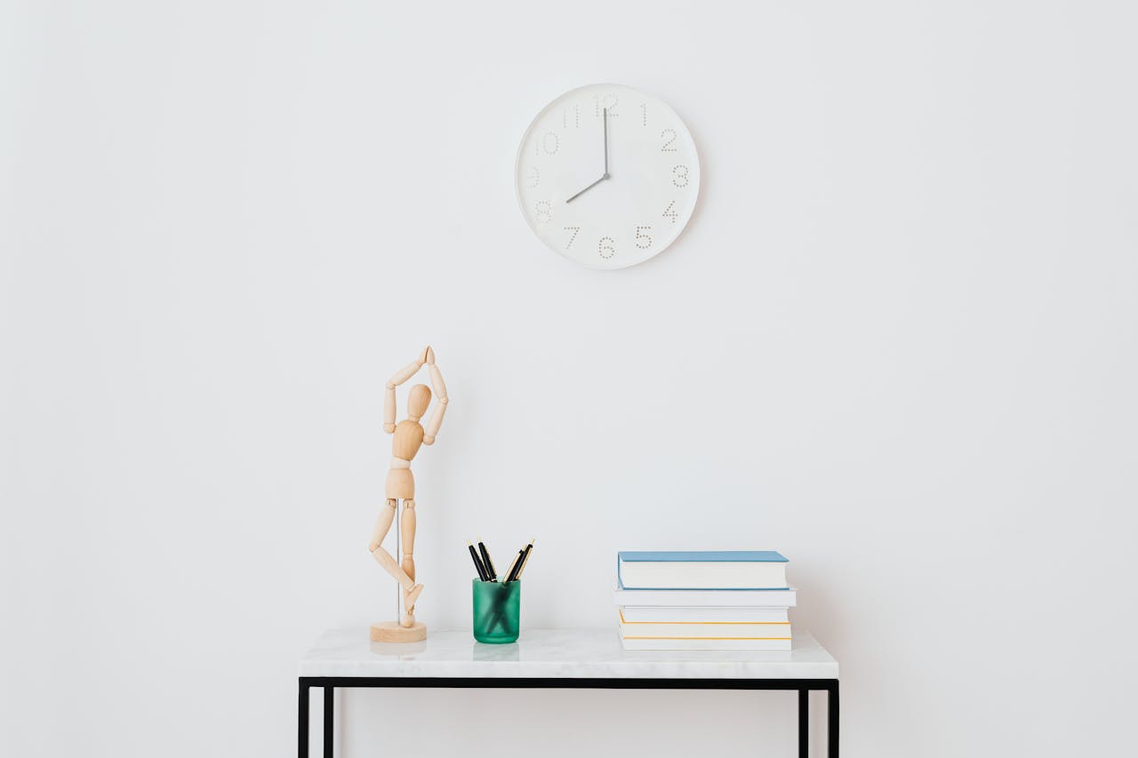A minimalist workspace setup featuring books, a clock, and decorative elements on a white wall.