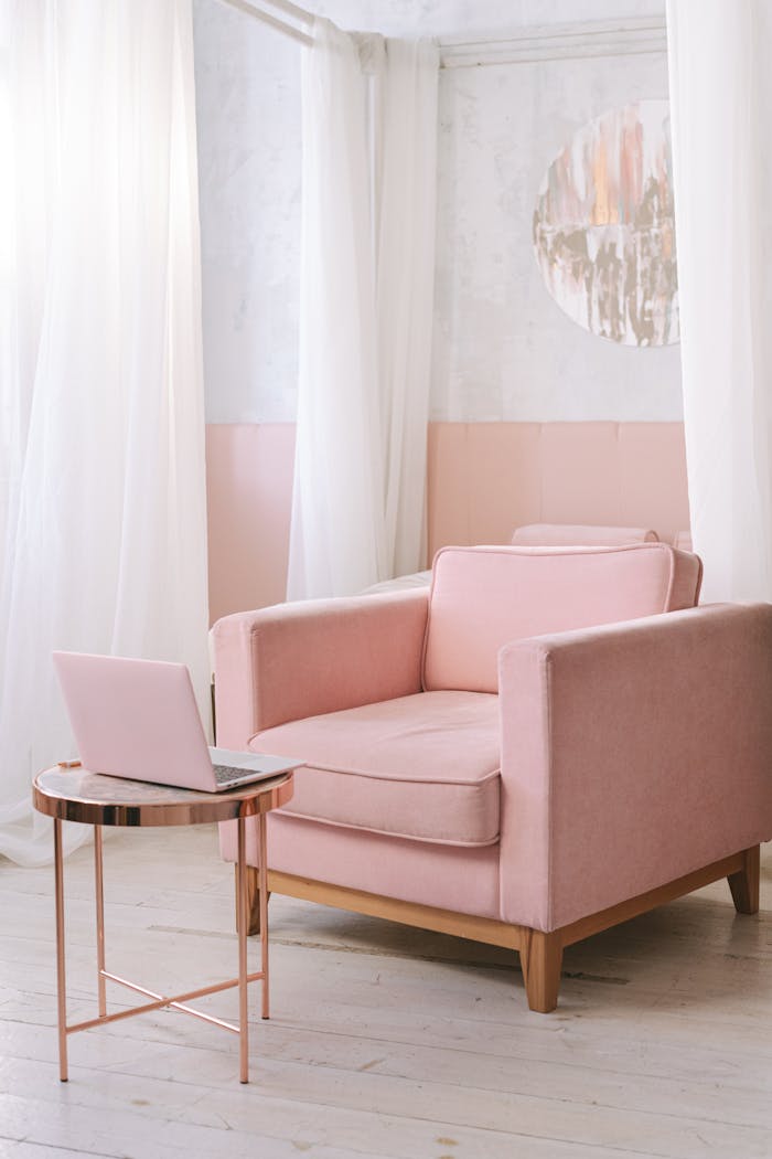 A chic pink armchair in a bright, modern living room with a laptop on the side table.